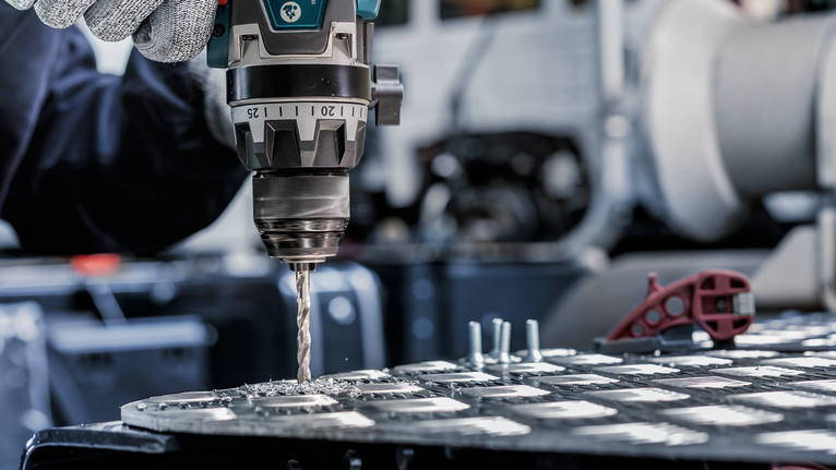 一名佩戴安全设备的人员在金属板上钻孔。