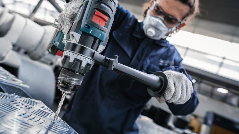 佩戴安全设备的人员使用电动工具钻入纹理金属。