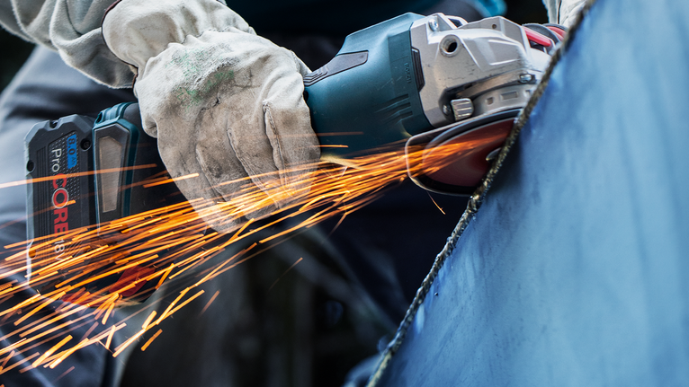 佩戴安全设备的人研磨金属，产生明亮的火花。