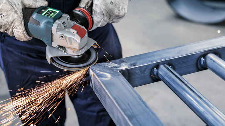 一名佩戴安全设备的人正在研磨金属框架，产生明亮的火花。