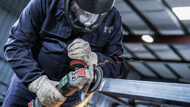 一名佩戴安全设备的人正在研磨金属，产生火花。