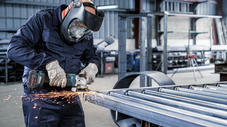 一名佩戴安全设备的人员在车间研磨金属，产生火花。