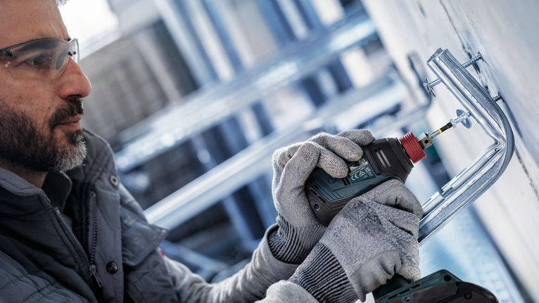 工人穿着安全设备，正在钻墙上安装的金属支架。