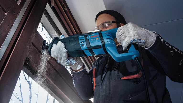 一名佩戴安全设备的人员使用往复锯切割木制窗框。