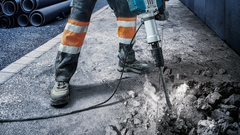 一名佩戴安全设备的人员使用手提钻凿破混凝土路面。
