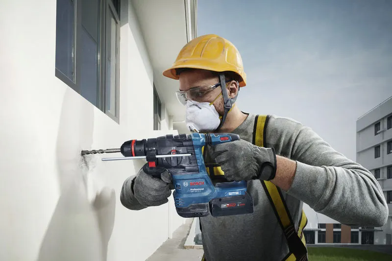 一名佩戴安全设备的人员使用电动工具在外墙上钻孔。.