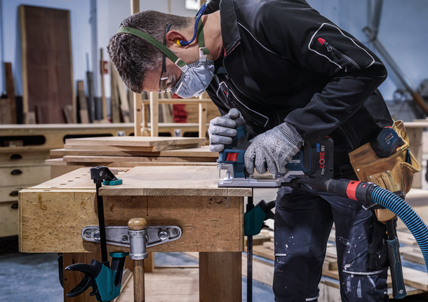佩戴安全设备的人员使用电动工具在工作台上切割木材。