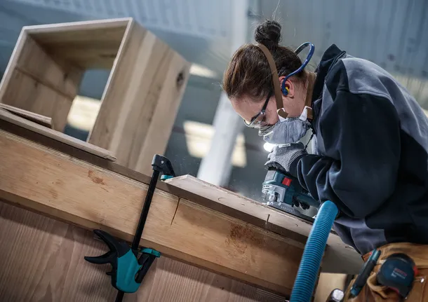 穿着安全设备的人员在车间使用电动工具对木材进行加工。