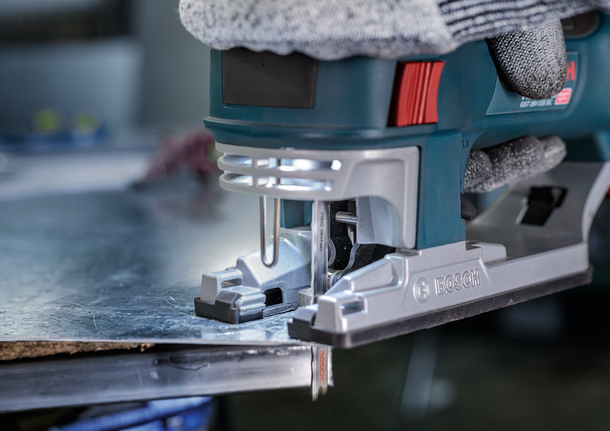 佩戴安全设备的人员使用曲线锯切割金属板。