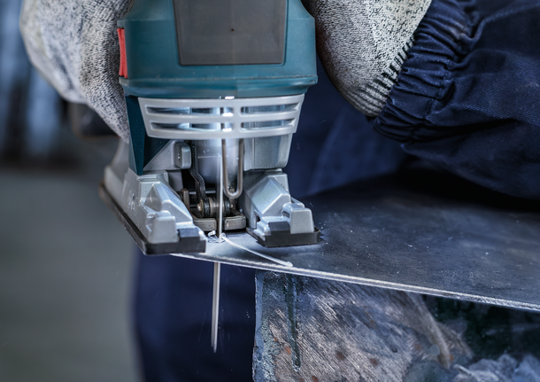 佩戴安全设备的人员用曲线锯切割金属板。