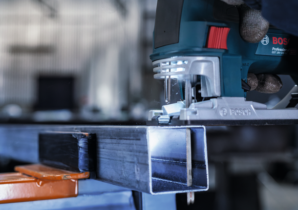 佩戴安全设备的人员引导曲线锯切割金属梁。