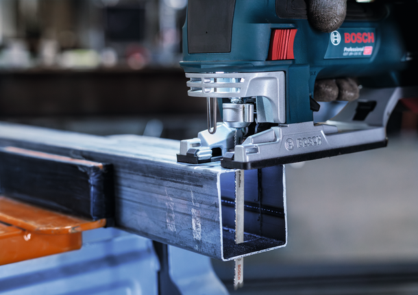 佩戴安全设备的人员用曲线锯切割金属梁。