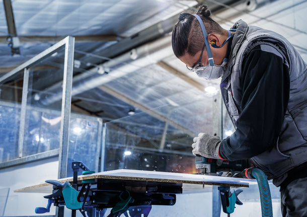 佩戴安全设备的人员使用电动工具切割木板。