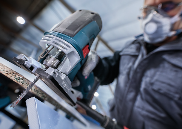 佩戴安全设备的人员使用曲线锯切割一块材料。