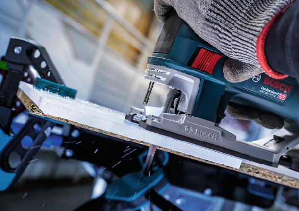 一名佩戴安全设备的人使用曲线锯切割一块木板。