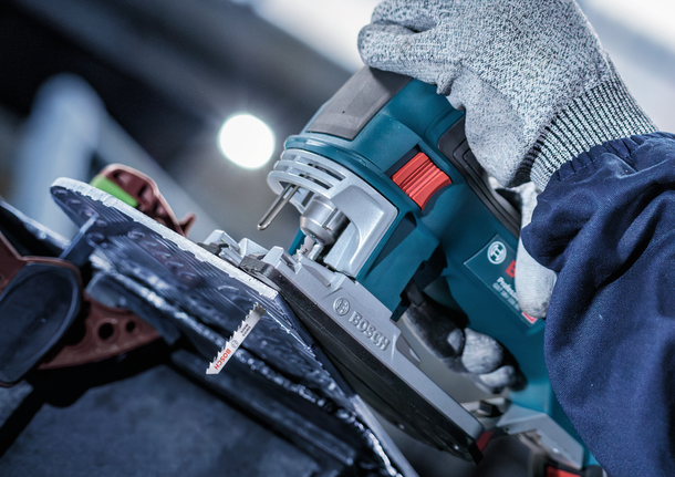 佩戴安全设备的人员使用曲线锯切割片状材料。