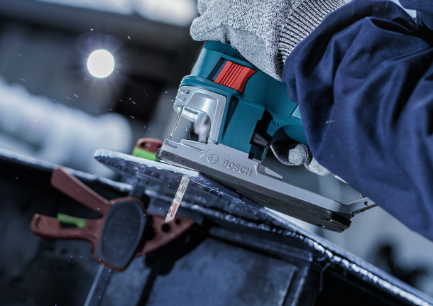 一名佩戴安全设备的人使用曲线锯切割金属板。