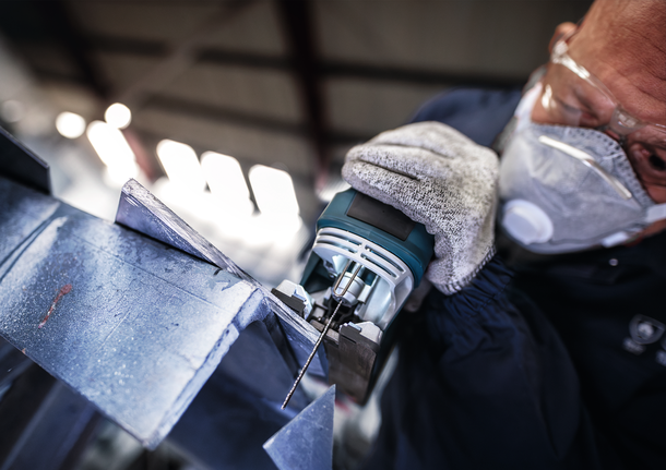 佩戴安全设备的人员使用曲线锯切割金属板。