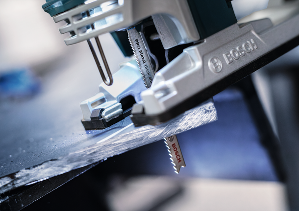 车间里，拼图锯正在切割一块深色金属板。