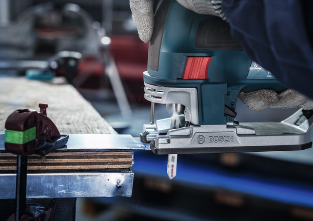 佩戴安全设备的人员用曲线锯切割金属板。