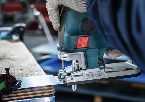 一名佩戴安全设备的人使用曲线锯切割金属板。