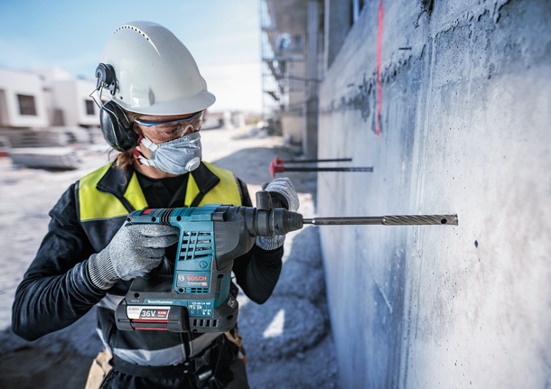 一名佩戴安全设备的人员在建筑工地的混凝土墙上钻孔。