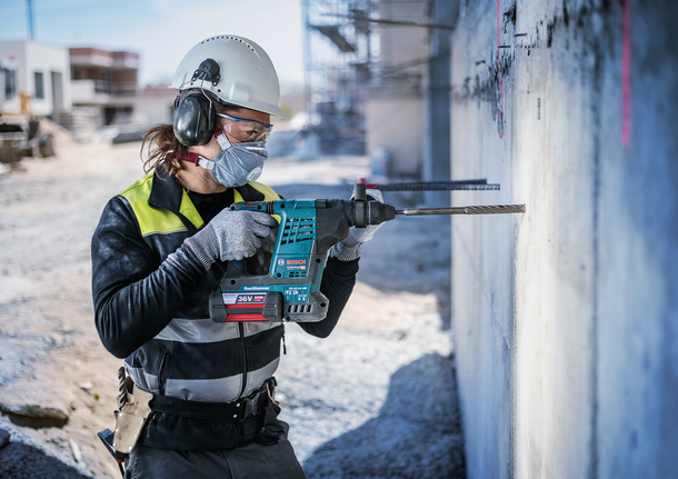 一名佩戴安全设备的人员在建筑工地的混凝土墙上钻孔。