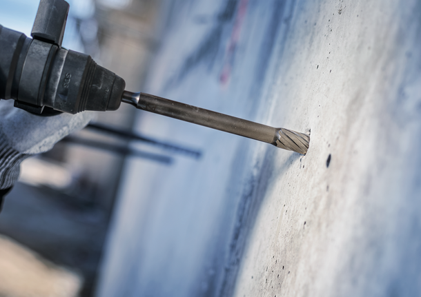 佩戴安全设备的人员使用旋转锤钻入混凝土。