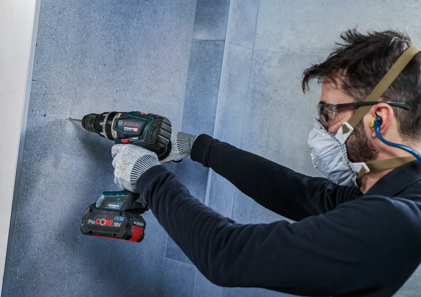 佩戴安全设备的人员正在向瓷砖墙上钻孔。