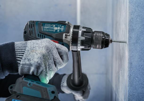 佩戴安全设备的人将螺丝钻入墙壁。