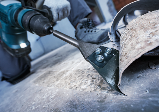 一名佩戴安全设备的人员使用电动工具拆除地板。