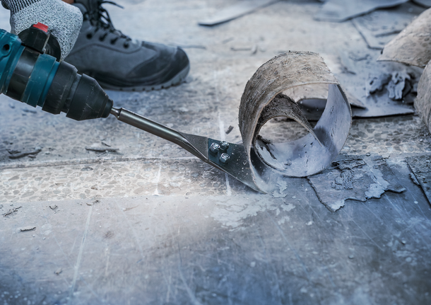 一名佩戴安全设备的人员使用电动工具刮擦地板材料。