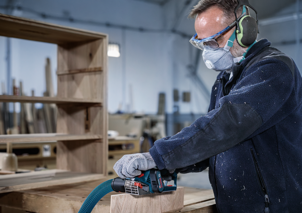 一名佩戴安全设备的工人在车间打磨木板。