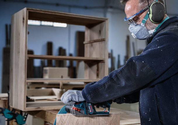 佩戴安全设备的人员使用电动工具打磨木制家具。