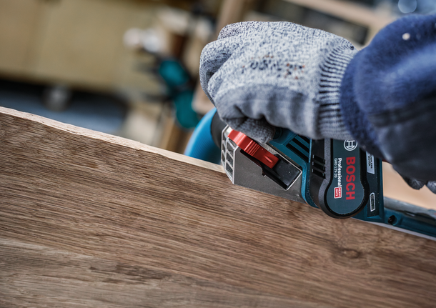 佩戴安全设备的人员使用电动工具打磨木板的边缘。