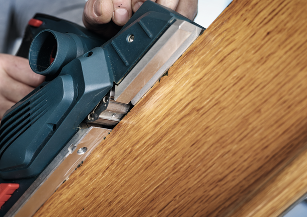 一个人使用电刨来打磨木板的边缘。