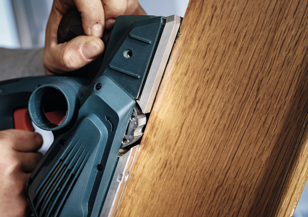 一个人使用电刨来打磨木板的边缘。