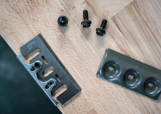 金属刀片、紧固螺钉和安装板排列在木质表面上。
