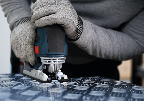 佩戴安全设备的人员使用曲线锯切割有图案的金属。