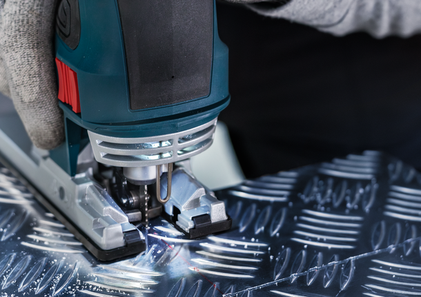 一名佩戴安全设备的人使用曲线锯切割有图案的金属。