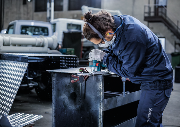穿着安全设备的人员在工业车间的工作台上钻金属。