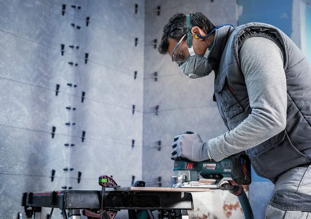 一名佩戴安全设备的人员在工作台上使用曲线锯切割木材。