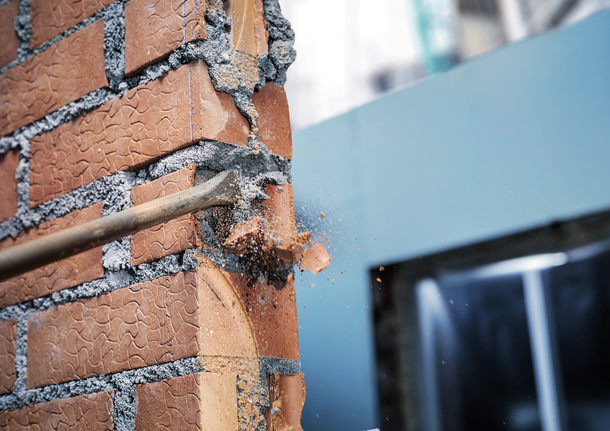 拆除锤正在拆除建筑工地上的一堵红砖墙。