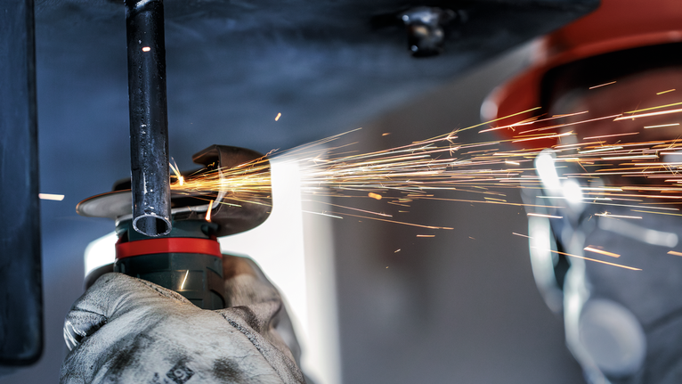 佩戴安全设备的人员在火花飞溅的情况下研磨金属管。.