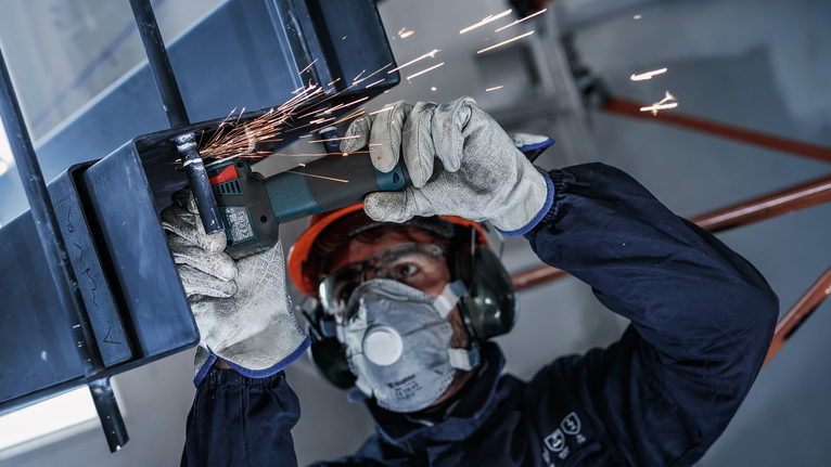 一名佩戴安全设备的人正在研磨金属，产生火花。