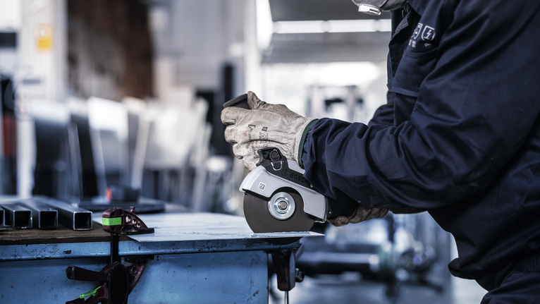 一名佩戴安全设备的人使用角磨机切割金属。