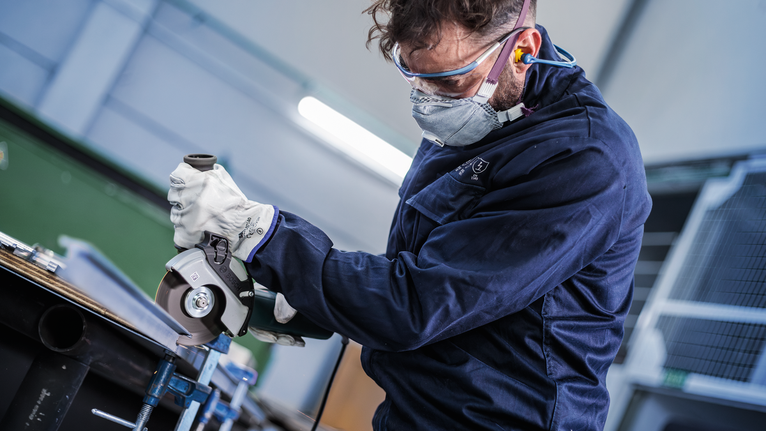 一名佩戴安全设备的人使用角磨机切割金属。