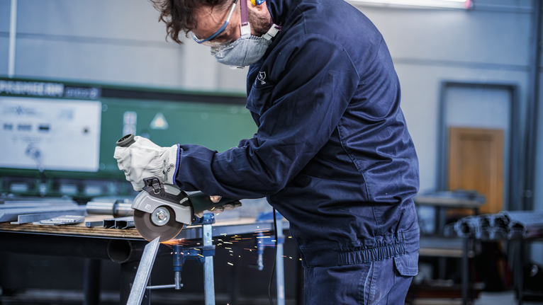 一名佩戴安全设备的人使用角磨机切割金属，产生火花。