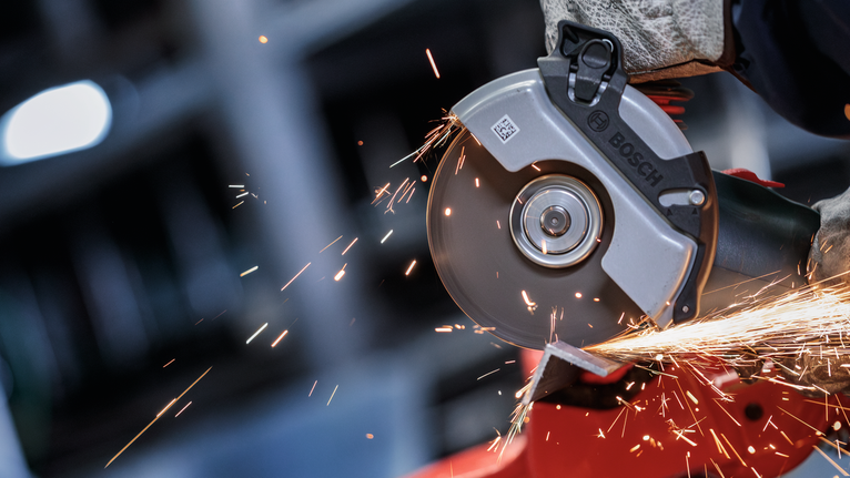 一名佩戴安全设备的人研磨金属，产生明亮的火花。