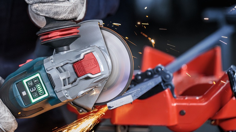 佩戴安全设备的人员使用角磨机切割金属棒。